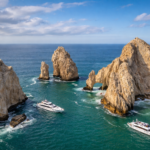 Aerial view of El Arco rock formations at Land’s End in Cabo San Lucas with two boats passing through turquoise water between the cliffs.